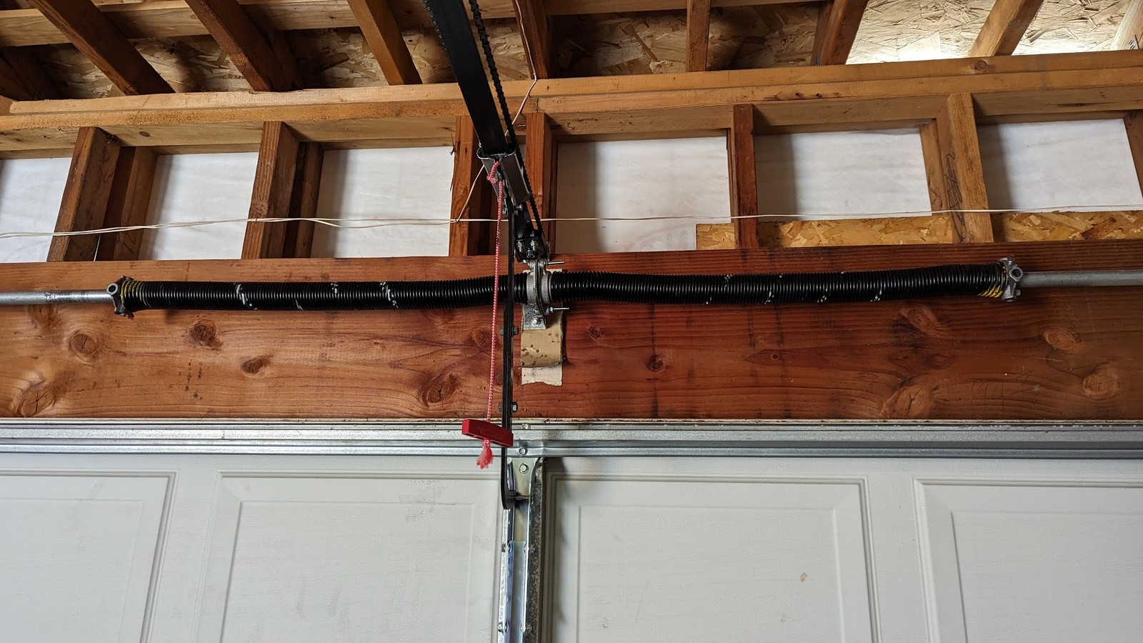 Garage door torsion spring shaft and opener rail above a sectional door